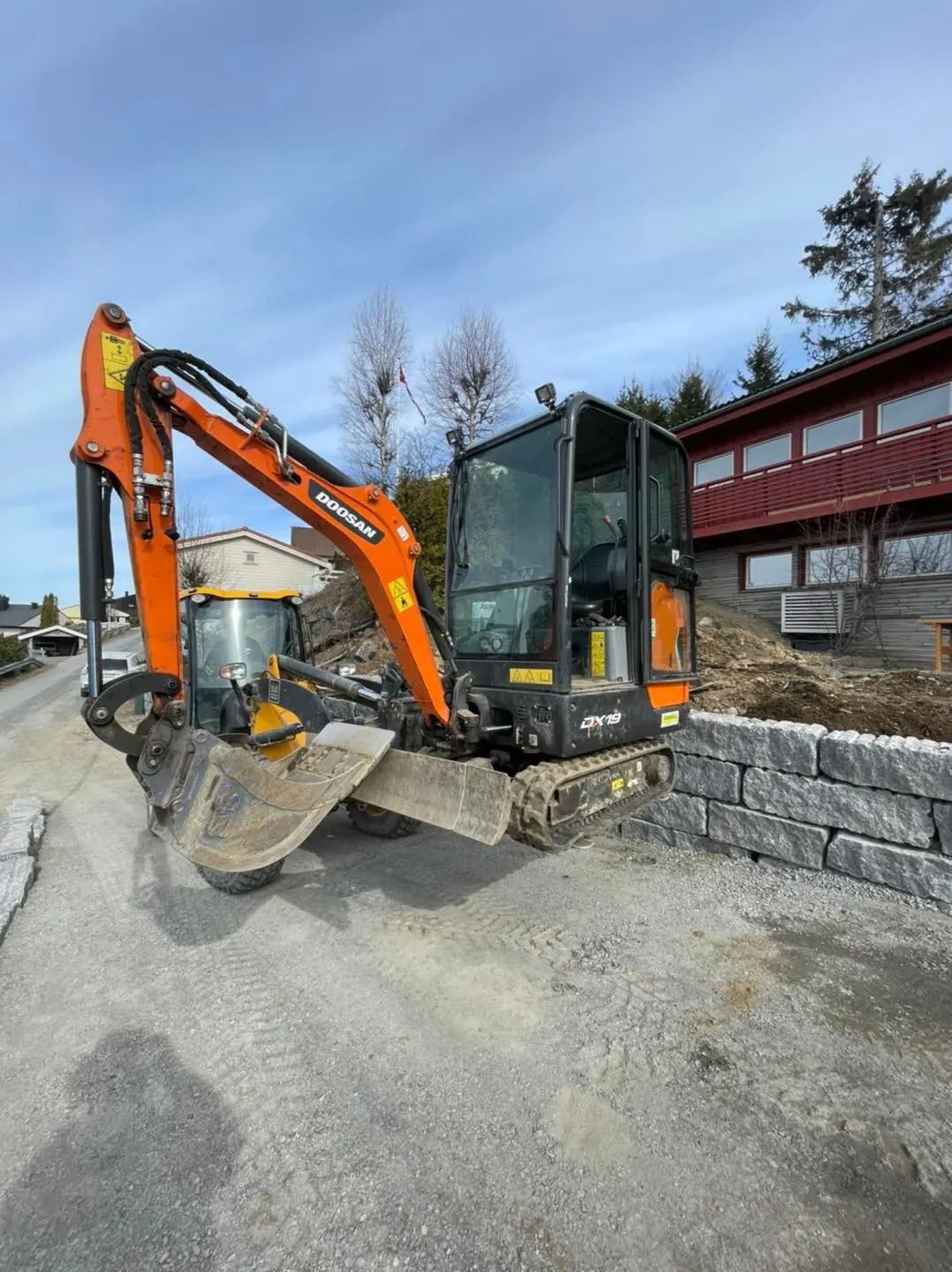 Gravemaskin i arbeid ved ferdig støttemur